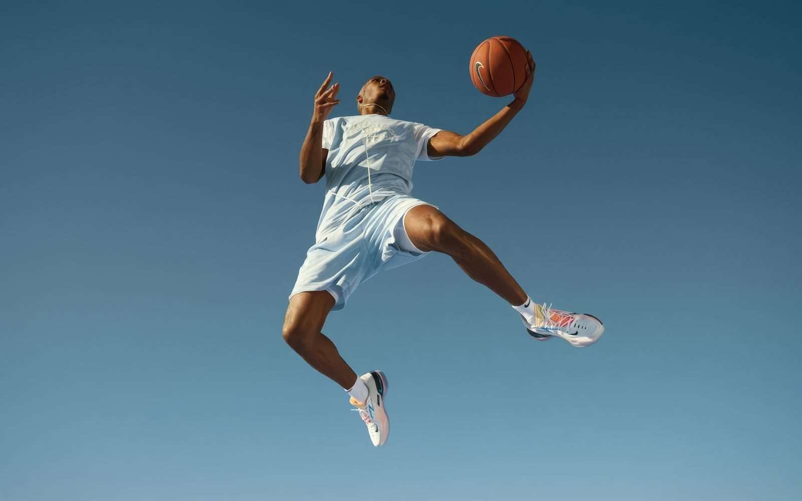 Basketball player mid-air dunk against a blue sky